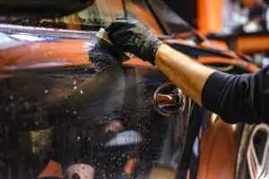 A person in black gloves cleaning the side of an orange car.